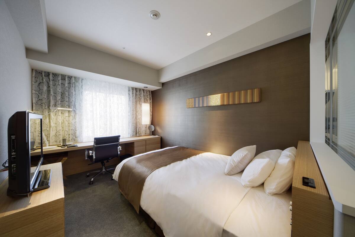 Une chambre d’hôtel moderne avec un grand lit, un bureau équipé d’un ordinateur et une fenêtre avec des rideaux.