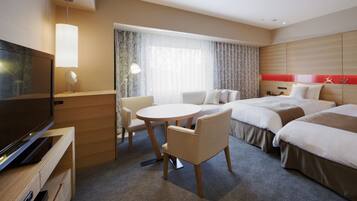 Habitación de hotel con televisión, una mesa redonda, dos camas, una silla y una ventana con cortinas.