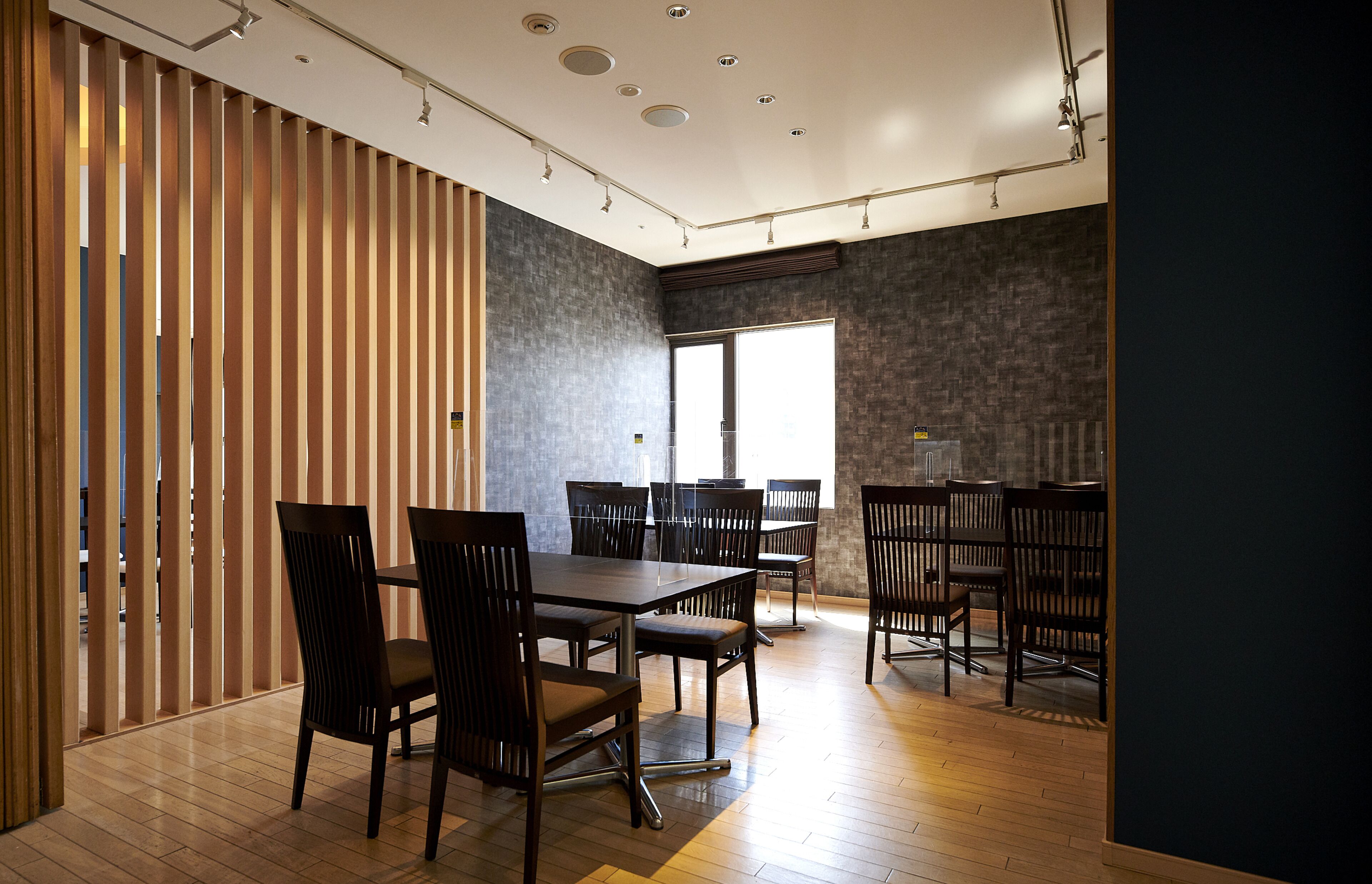 Una sala de reuniones moderna con un separador de madera, una mesa grande con sillas y vistas al exterior a través de un ventanal.