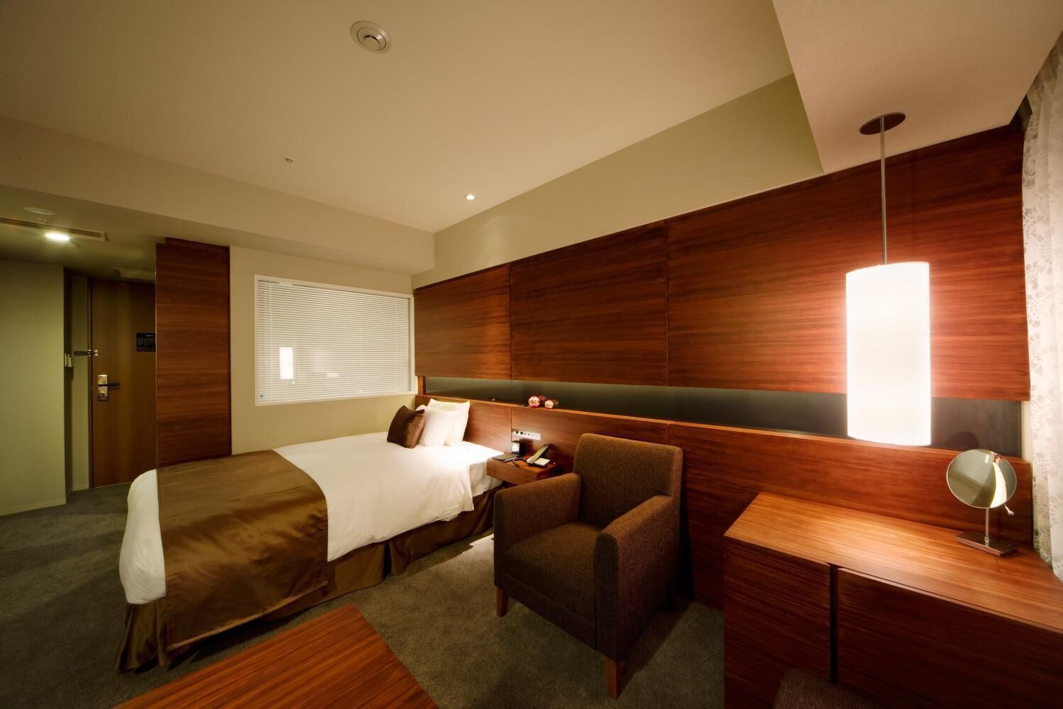 A hotel room with a bed, a desk, a chair, and a bedside table.