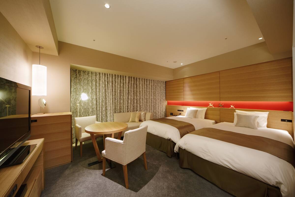Une chambre d’hôtel équipée d’une télévision, d’un bureau, d’une table ronde, d’un canapé et de deux lits.
