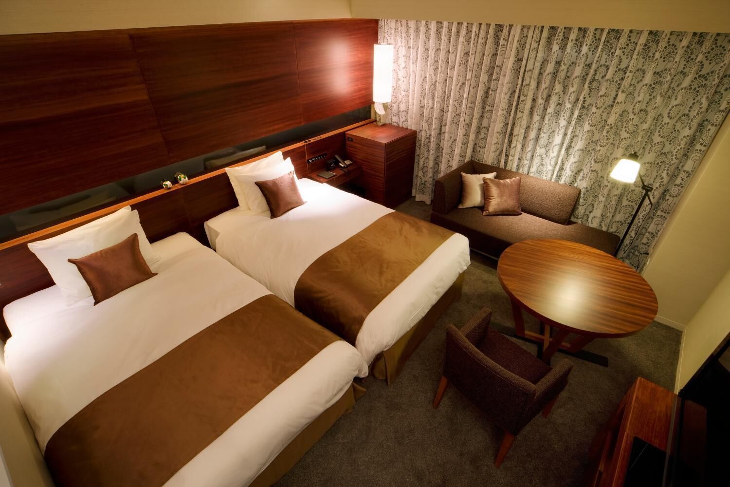 Een hotelkamer met twee bedden, een bank, een tafeltje en een lamp.