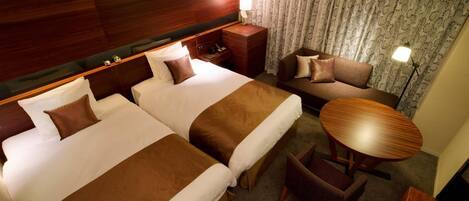 A hotel room with two beds, a sofa, a small table, and a lamp.