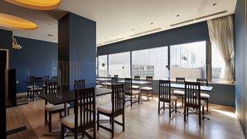 Un comedor moderno con múltiples mesas y sillas, ventanas amplias con vistas a la ciudad y una pared azul de acento.