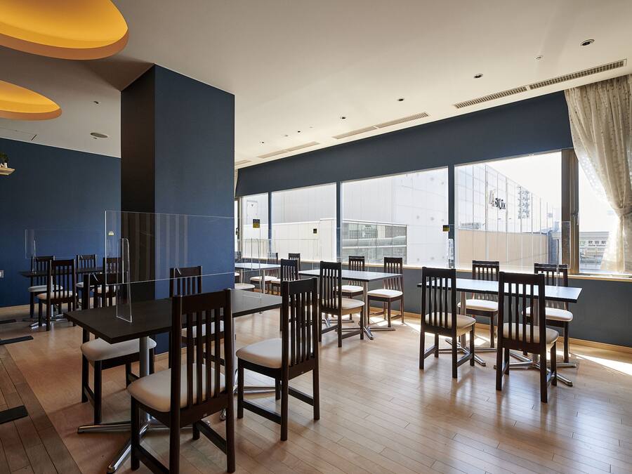 Un comedor moderno con múltiples mesas y sillas, ventanas amplias con vistas a la ciudad y una pared azul de acento.