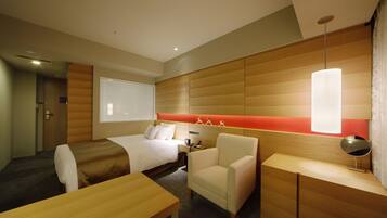 A hotel room with a bed, a desk, a chair, and a bedside table.