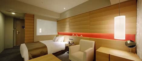 A hotel room with a bed, a desk, a chair, and a bedside table.