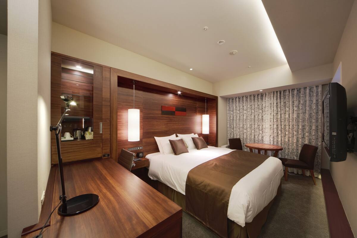 Une chambre d’hôtel moderne équipée d’un grand lit, d’un bureau, d’une chaise, d’une petite table et d’un téléviseur.