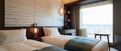 A hotel room with two beds, a large window with a city view, a wall with a textured pattern, and a hanging lamp.