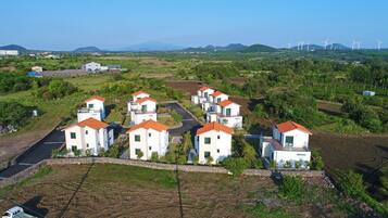 A residential area with modern houses, a paved road, and wind turbines in the background.