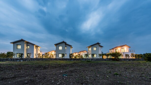 Una hilera de casas modernas con un muro de piedra al frente, bajo un cielo crepuscular.