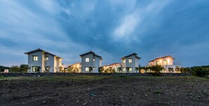 A row of modern houses with a stone wall in front, under a twilight sky.