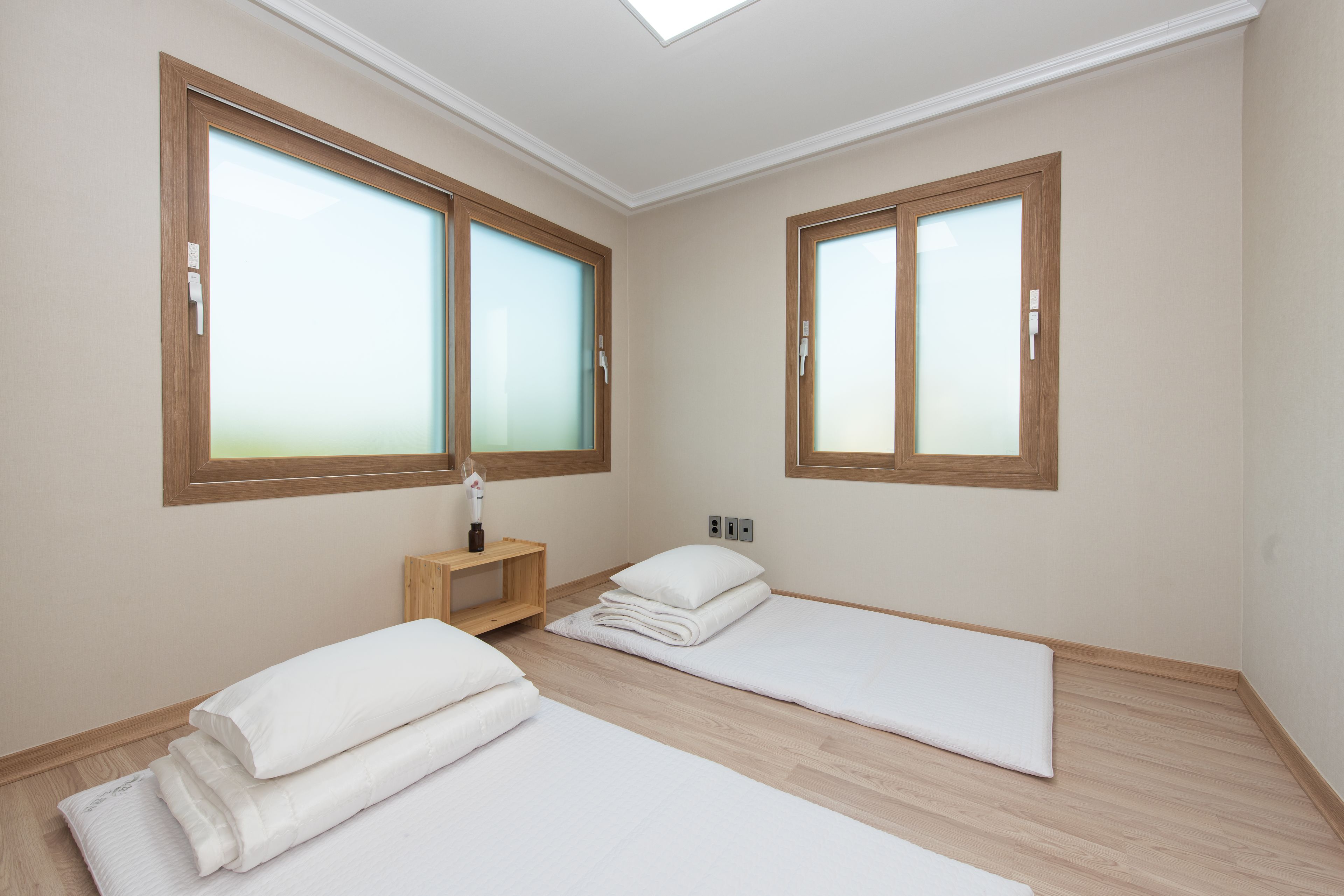 A room with two beds, wooden flooring, and large windows with frosted glass.