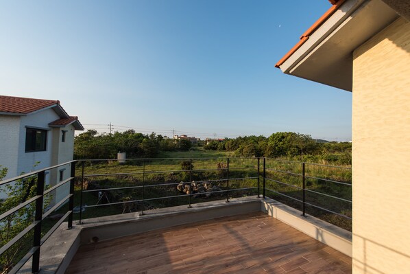 A balcony with a view of a grassy field and distant buildings.