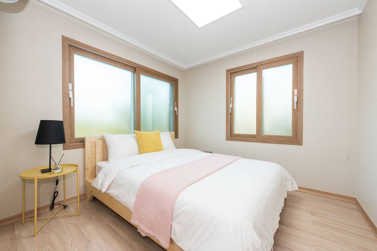 A bedroom with a bed, a bedside table with a lamp, and two windows with frosted glass.