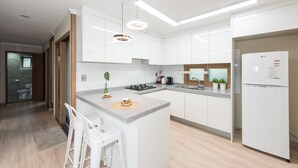 Una cocina moderna con armarios blancos, encimera de granito, horno empotrado, refrigerador e iluminación colgante.