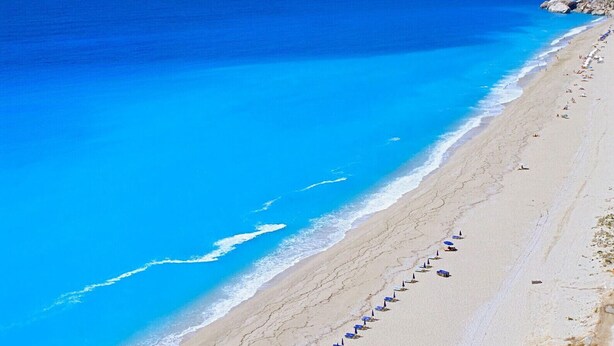 A beach with a row of blue umbrellas and lounge chairs along the shoreline.