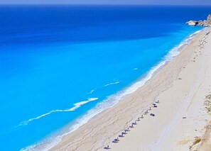 Ein Strand mit einer Reihe blauer Sonnenschirme und Liegestühlen entlang der Küste.