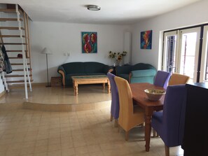 A living room with a sofa, a coffee table, and a dining table with chairs. There is a staircase with a handrail and a lamp. - House (140m2, 3 large bedrooms), garden (800m2) fenced, great (Orfu)