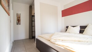 Een moderne slaapkamer met een bed, een rode accentmuur en een schilderij aan de muur.