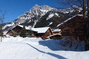 Un chalet de montagne avec des cabanes en bois, des toits enneigés et, en arrière-plan, des sommets couverts de neige.