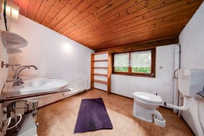 Une petite salle de bain avec un plafond en bois, un lavabo blanc, des toilettes et une fenêtre donnant sur un paysage verdoyant.