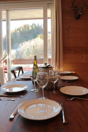 A dining table set with plates, wine glasses, and cutlery, with a bottle of wine and a basket of bread.