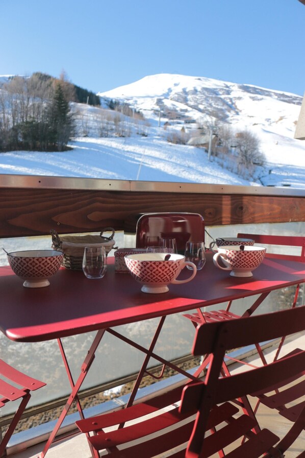 A wooden deck with a red table set for dining, overlooking a snowy mountain landscape.