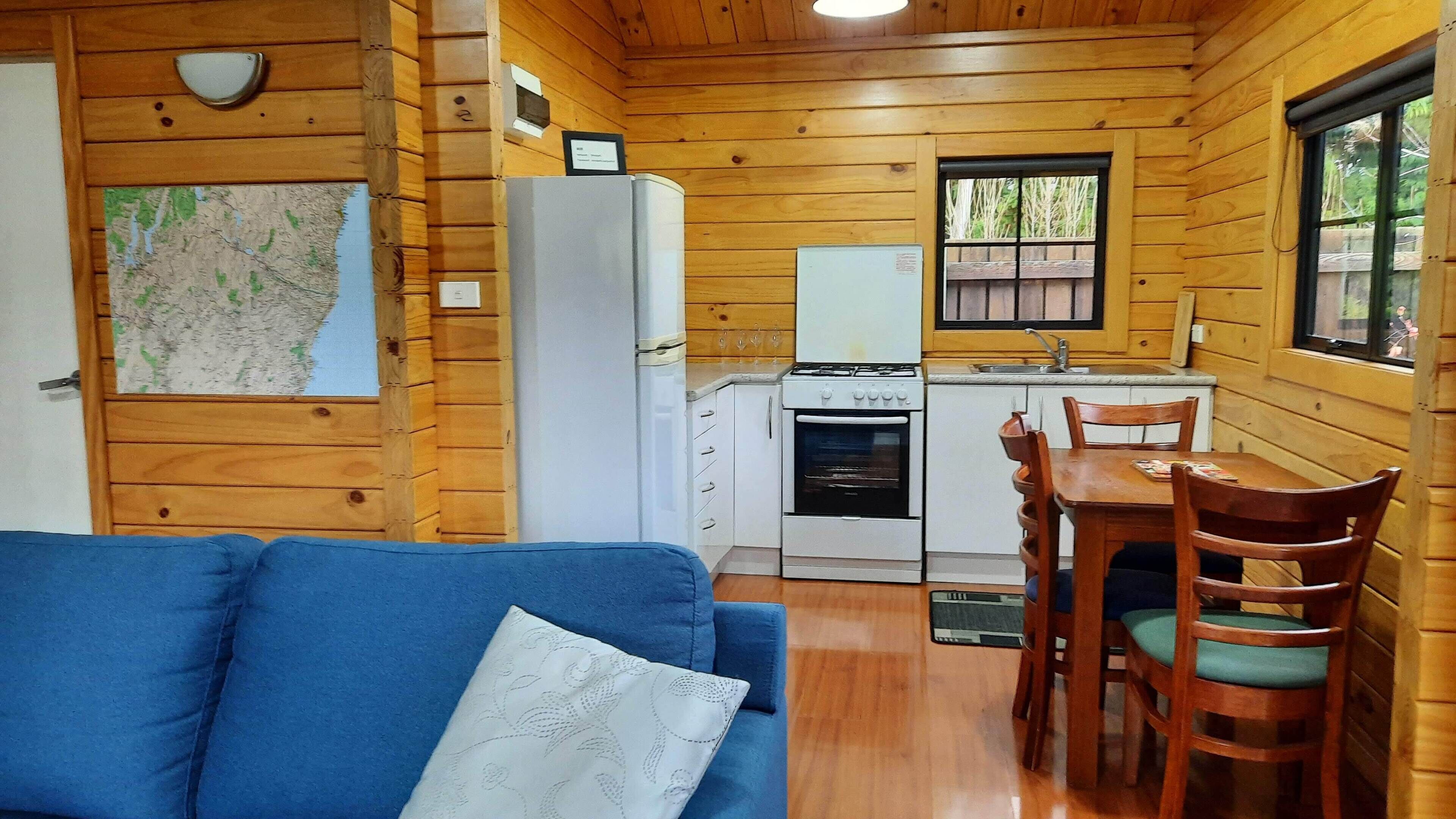 Ein Holzblockhaus-Interieur mit Küchenzeile, Essbereich und einem blauen Sofa.
