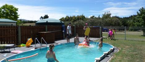A swimming pool with a wooden deck, a covered area, and a fenced yard.