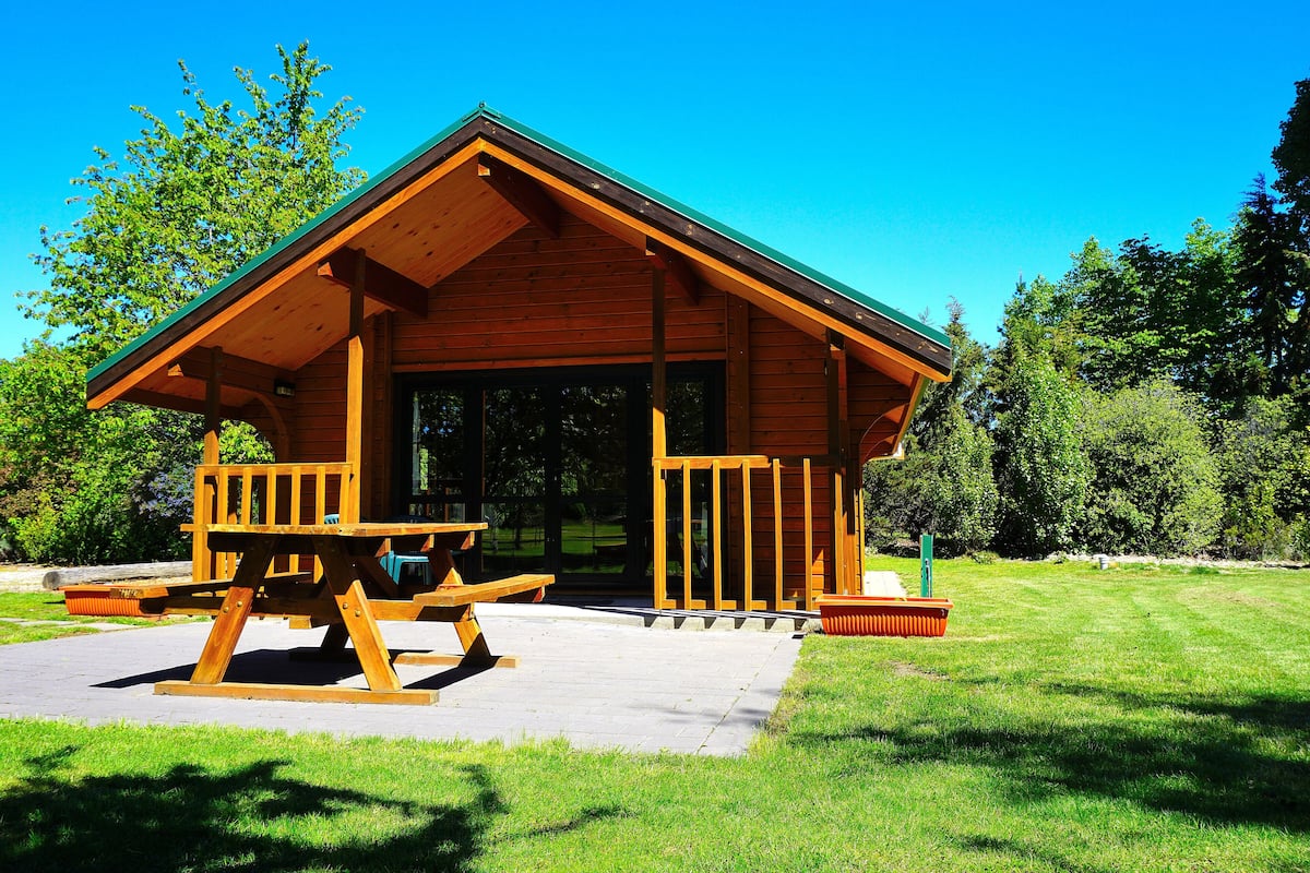 A wooden cabin with a porch, picnic table, and a grassy lawn.