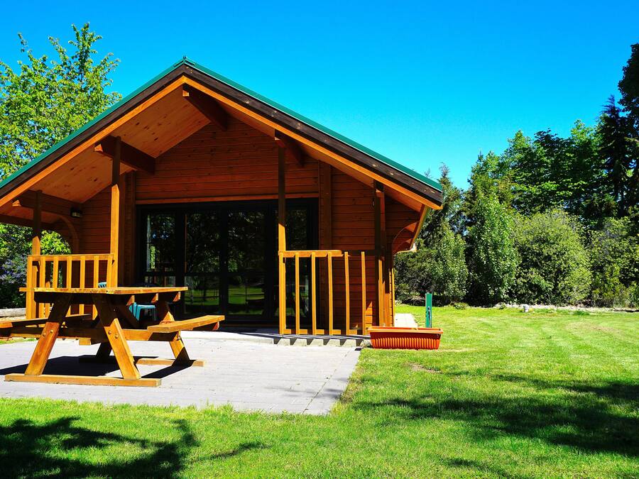 Una cabaña de madera con porche, mesa de picnic y césped.