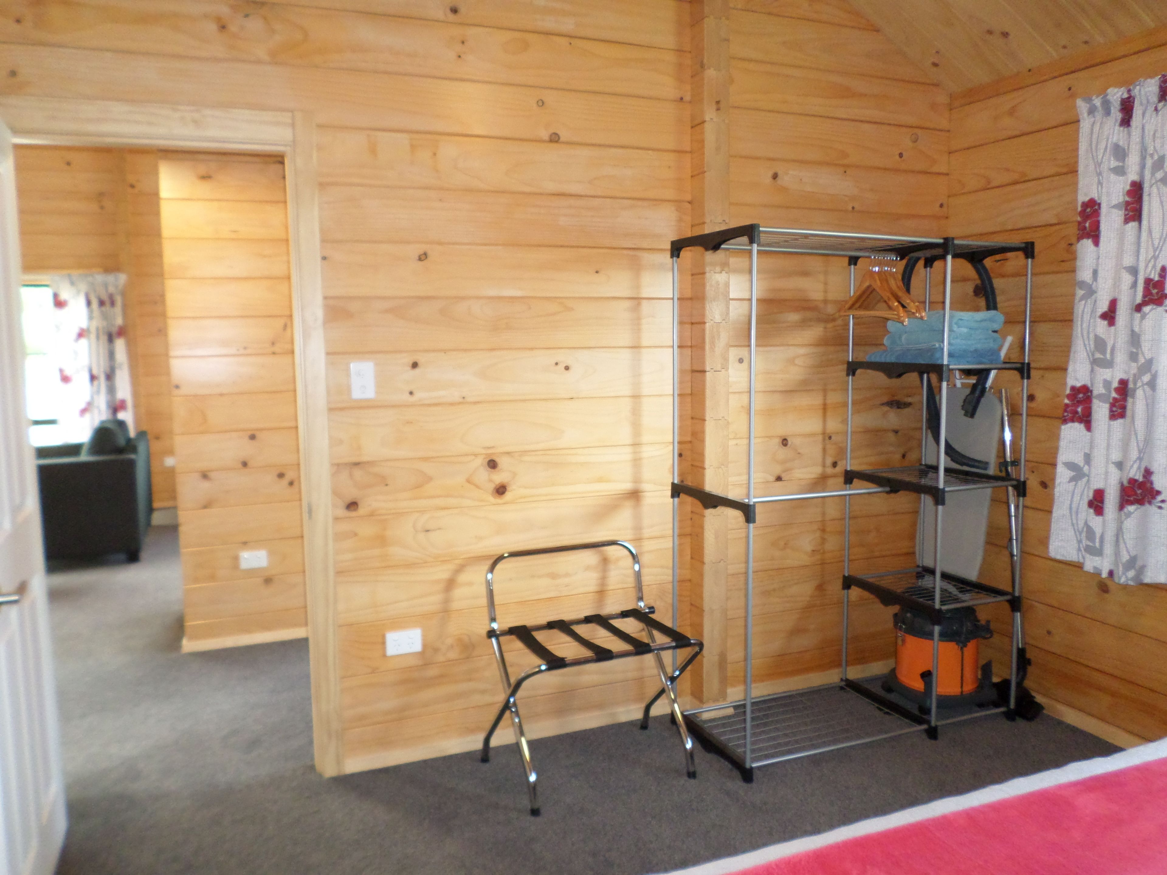 A wooden cabin interior with a metal shelf unit and a small bench.