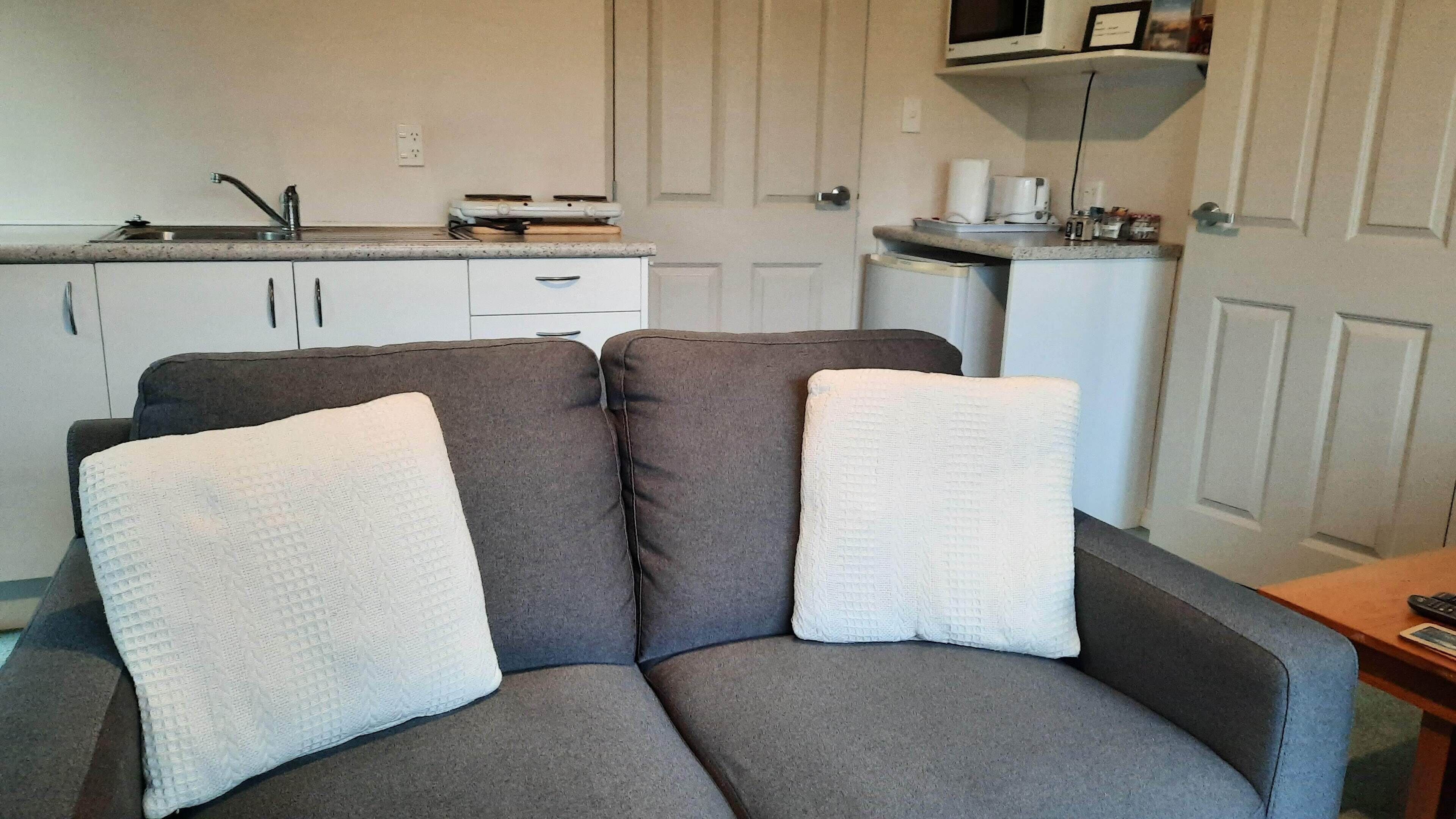 A gray sofa with two white cushions in a room with a kitchenette in the background.