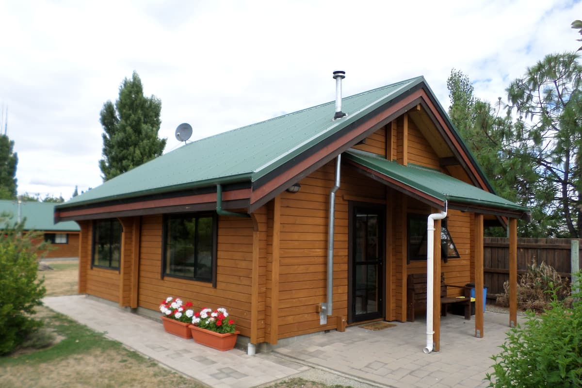 A wooden cabin with a green roof, large windows, and a covered porch.