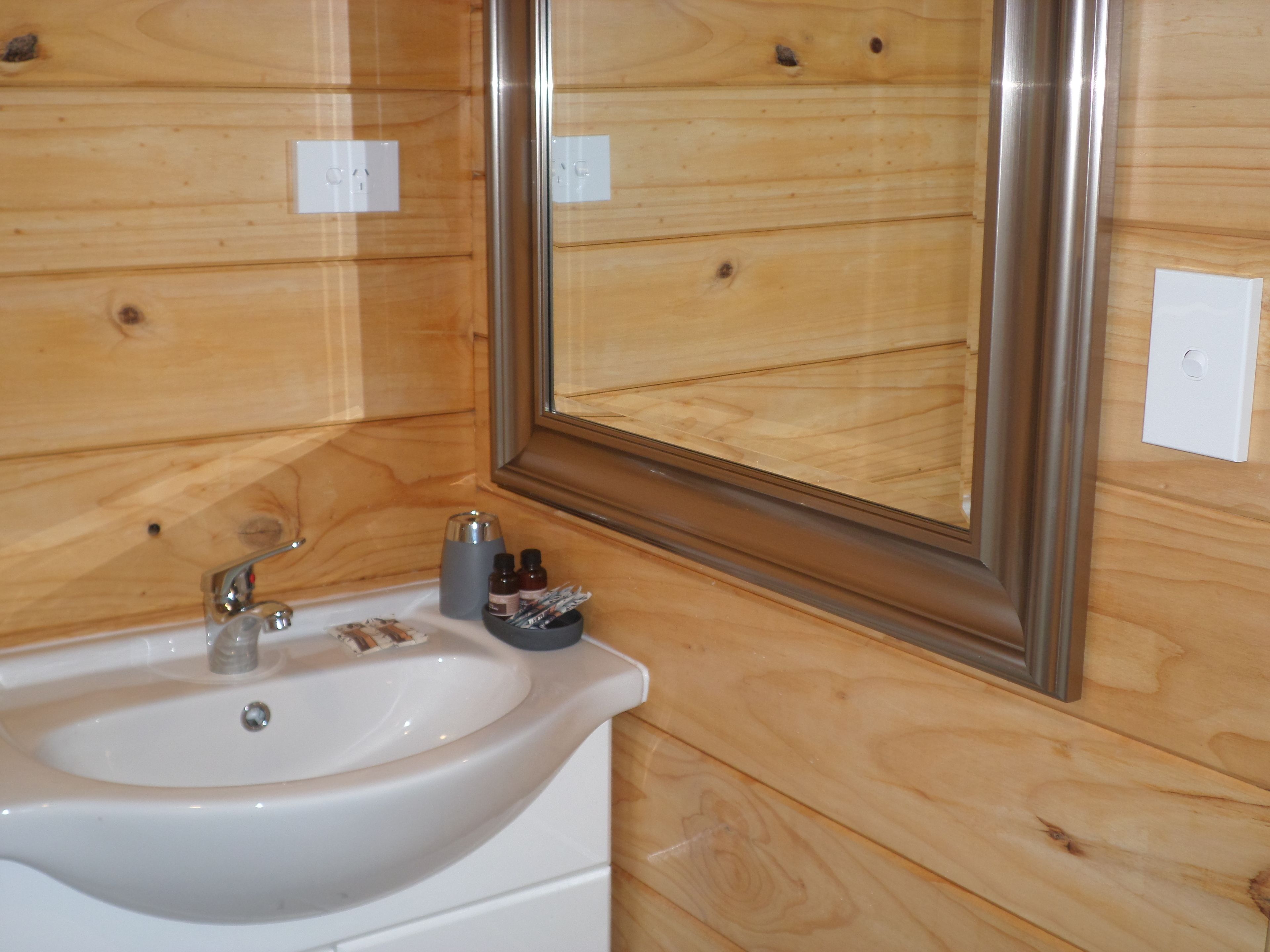 Un baño con pared de madera, un lavamanos blanco, un espejo y un grifo.