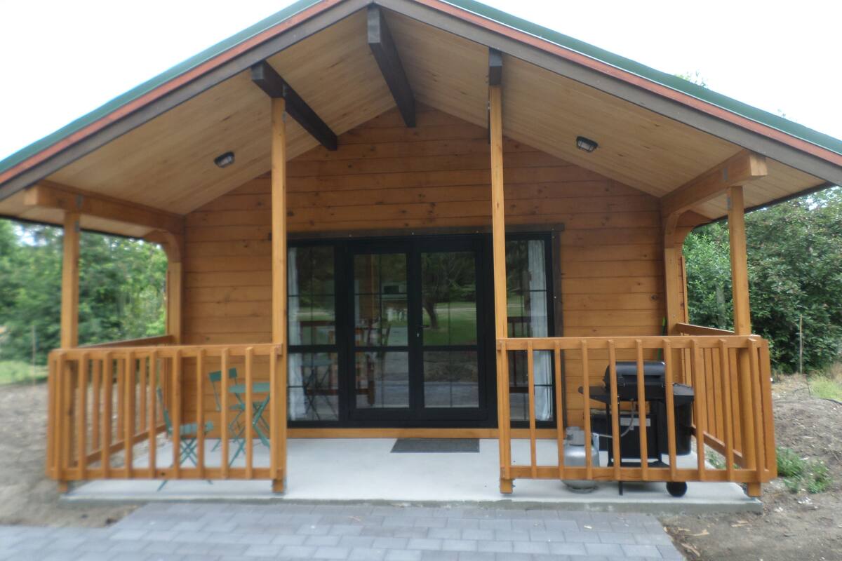 A wooden cabin with a porch, large windows, and a chimney.