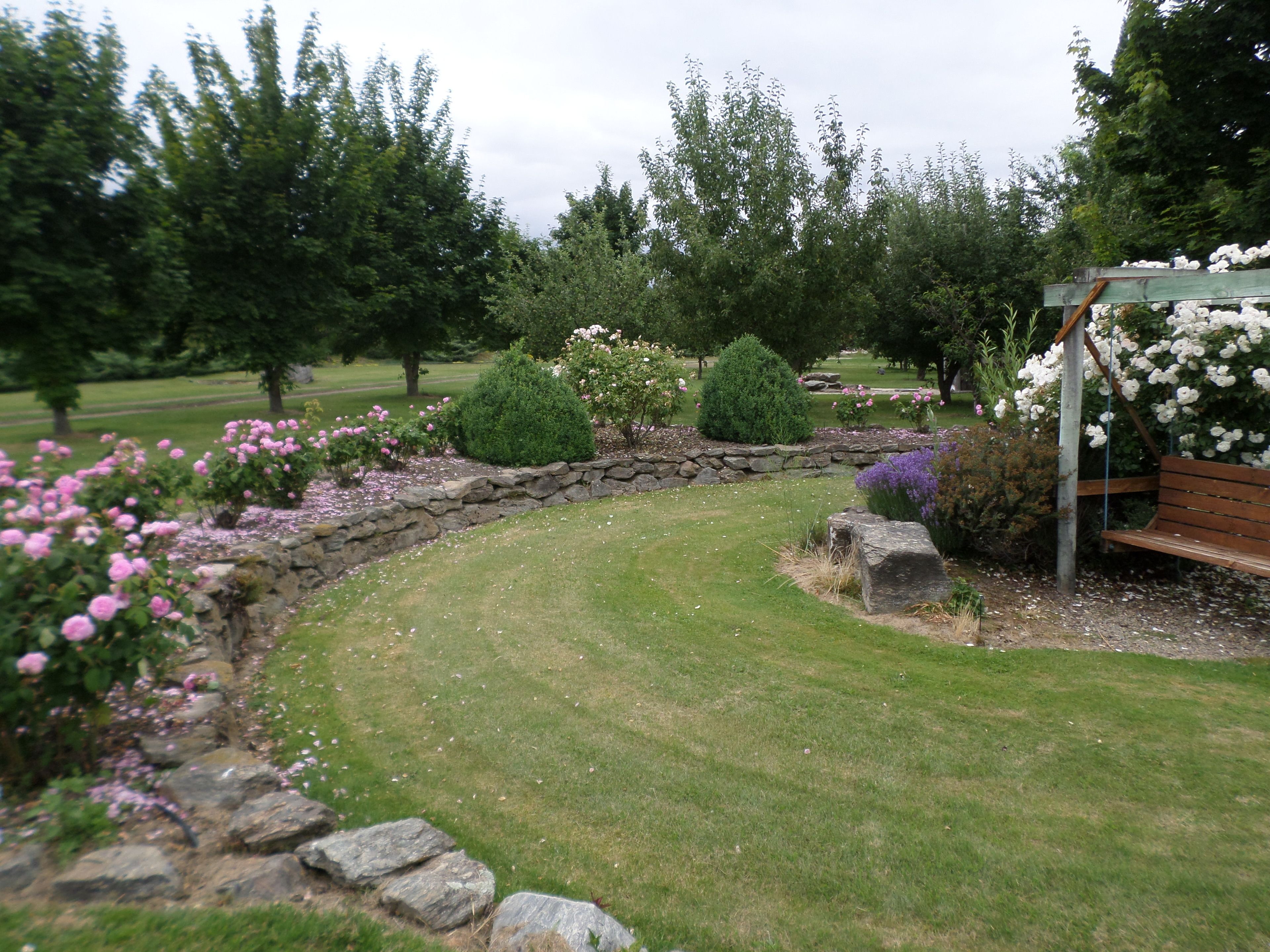 A landscaped garden with a stone wall, a wooden bench, and various flowering plants.