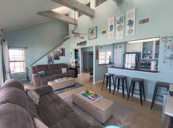 A spacious living area with a sofa, ottoman, and bar stools. A kitchen with a refrigerator and stove is visible.