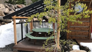En træpergola med et bord og bænke, omgivet af sten og sne.