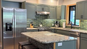 A modern kitchen with a stainless steel refrigerator, a built-in water dispenser, a gas stove, and a large island with bar stools.