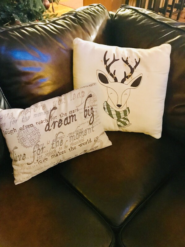 Un sofá de cuero marrón con dos almohadones decorativos, uno con una ilustración de un ciervo y el otro con texto estampado.