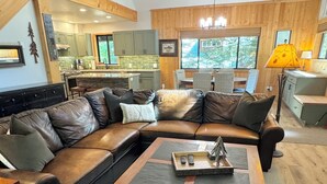 A spacious living room with a large sectional sofa, a wooden coffee table, and a kitchen area in the background.