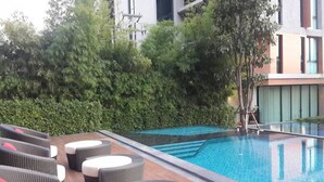 A swimming pool with a tiled deck, surrounded by greenery and modern buildings. - Sandao Condo Khaoyai (Pak Chong)