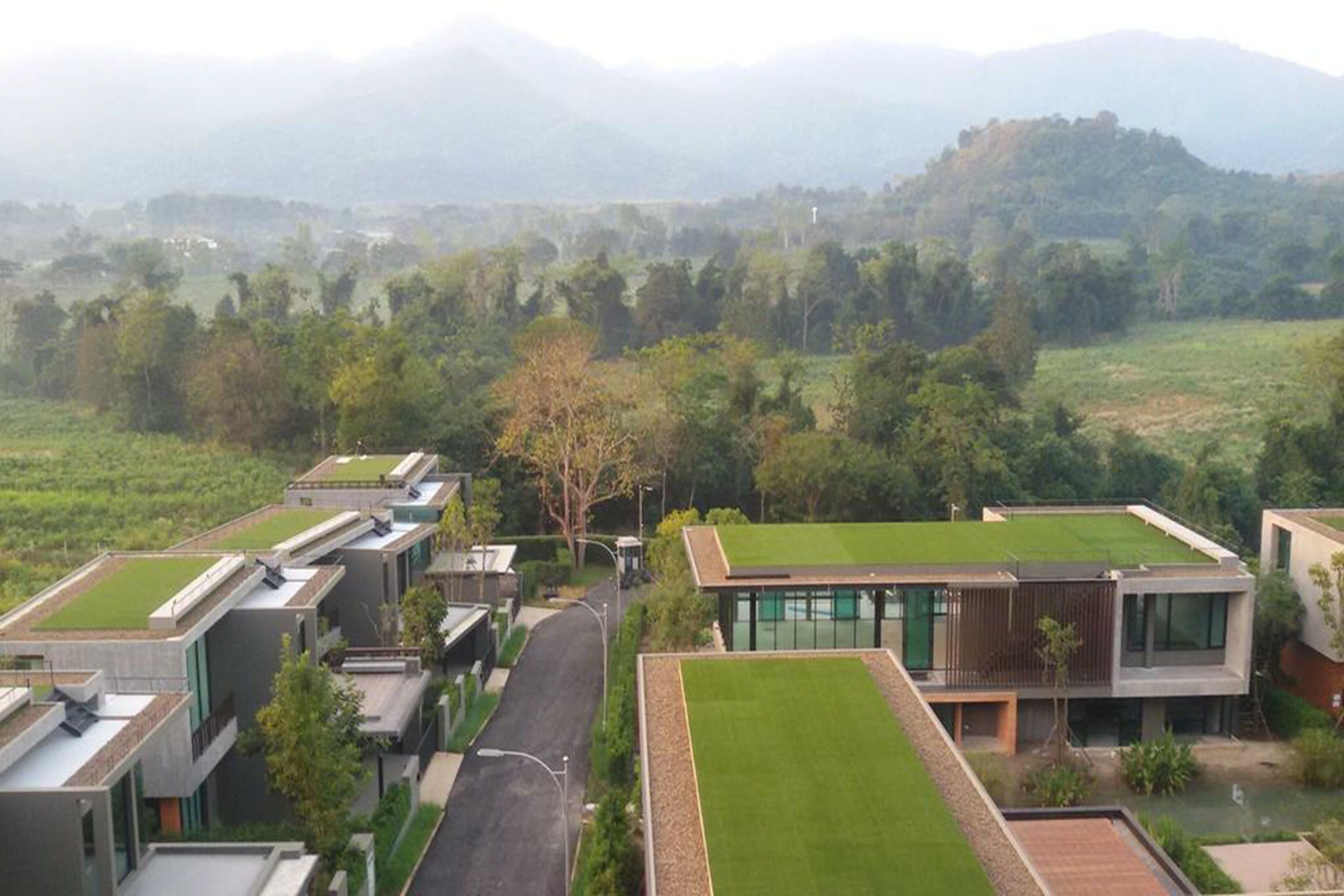 Un complexe résidentiel moderne composé d’immeubles à toits plats, de pelouses verdoyantes et d’un paysage vallonné en arrière-plan.
