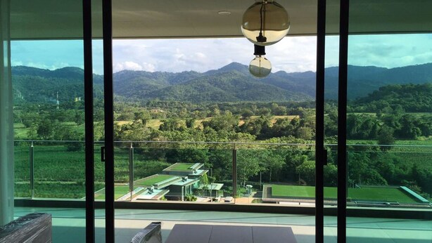 A room with large windows offering a view of a mountainous landscape and a green field. - Sandao Condo Khaoyai (Pak Chong)