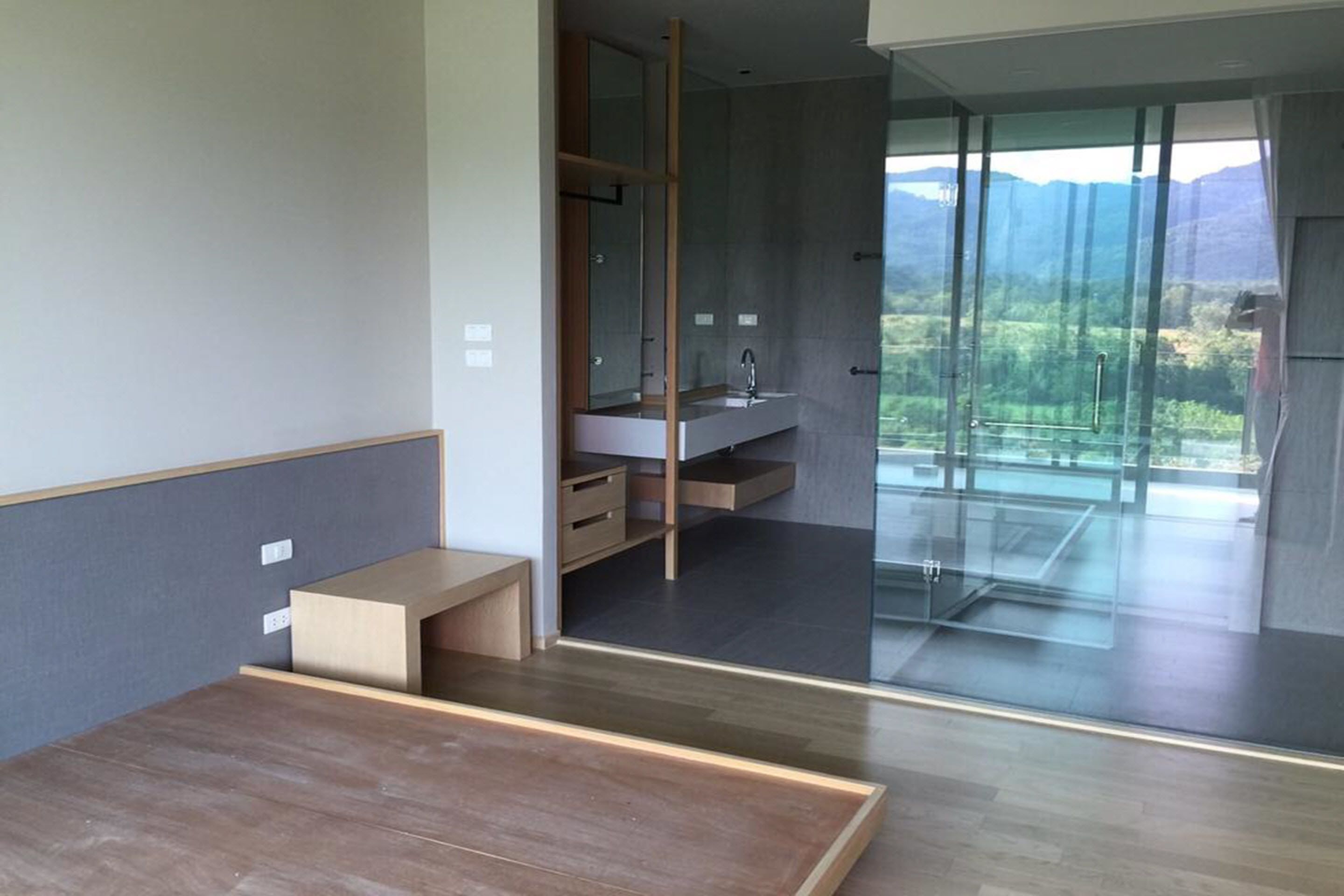 Uma casa de banho moderna com cabine de chuveiro em vidro, um banco de madeira e vista para uma paisagem montanhosa.