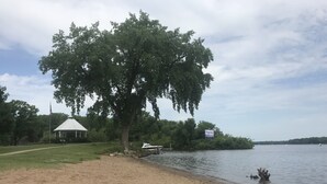 A sandy beach with a gazebo, a large tree, and a sign for 'Parkside'.