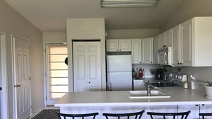 A kitchen with white cabinets, a central island with bar stools, a refrigerator, and a microwave.