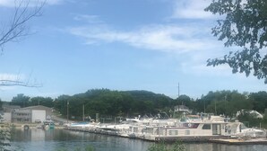 A marina with several boats docked, a building with a garage, and a hill with trees in the background.